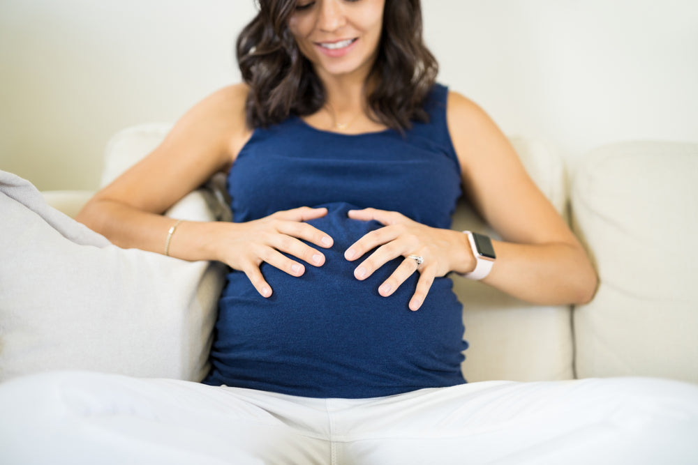 Pregnant woman sitting on couch holding belly | Nourish Baby