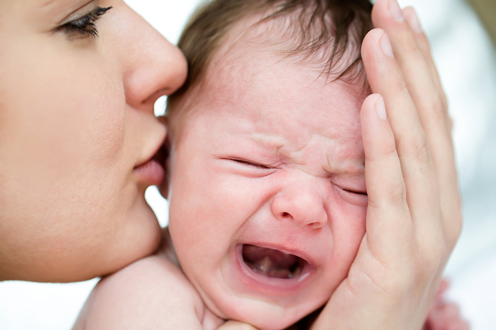 Mother kissing crying baby | Nourish Baby