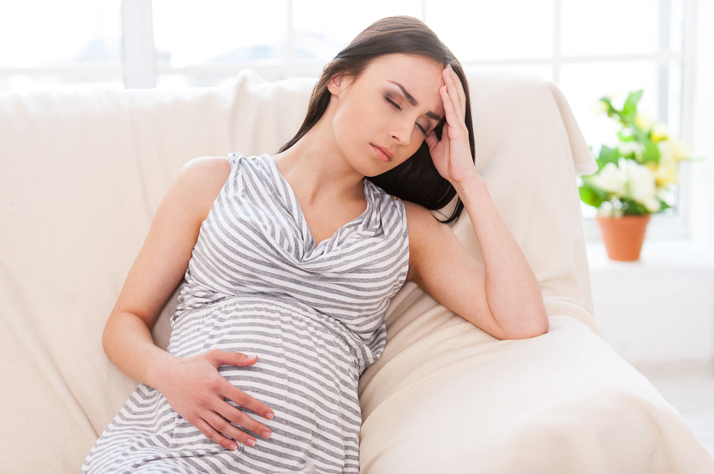 Pregnant woman sitting on couch with a headache | Nourish Baby