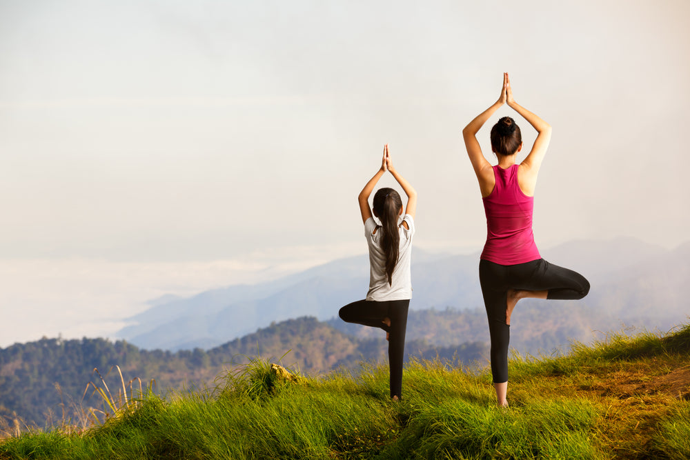 Mother and daughter doing yoga on a mountain top | Nourish Baby