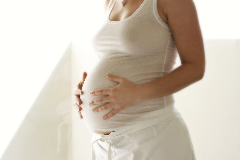 Woman in white singlet and pants holding baby bump | Nourish Baby