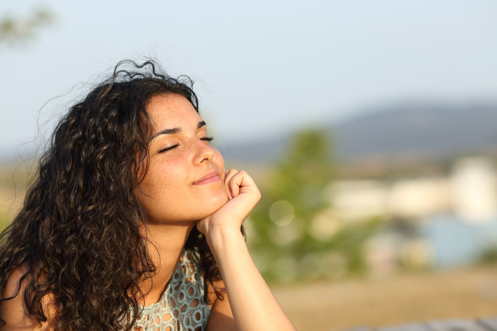 Content woman facing sun with eyes closed | Nourish Baby