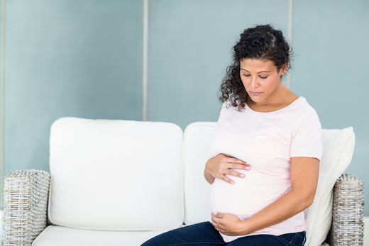Sad pregnant mother sitting on couch | Nourish Baby