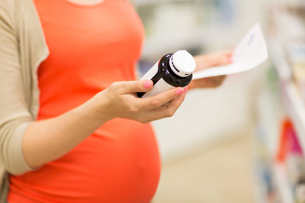 Pregnant mother looking at a bottle of pills | Nourish Baby