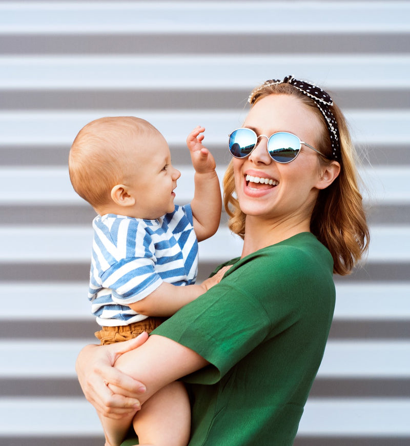 A girl wear a blue sun glasses with green color top and carry a baby in her hand , and the baby